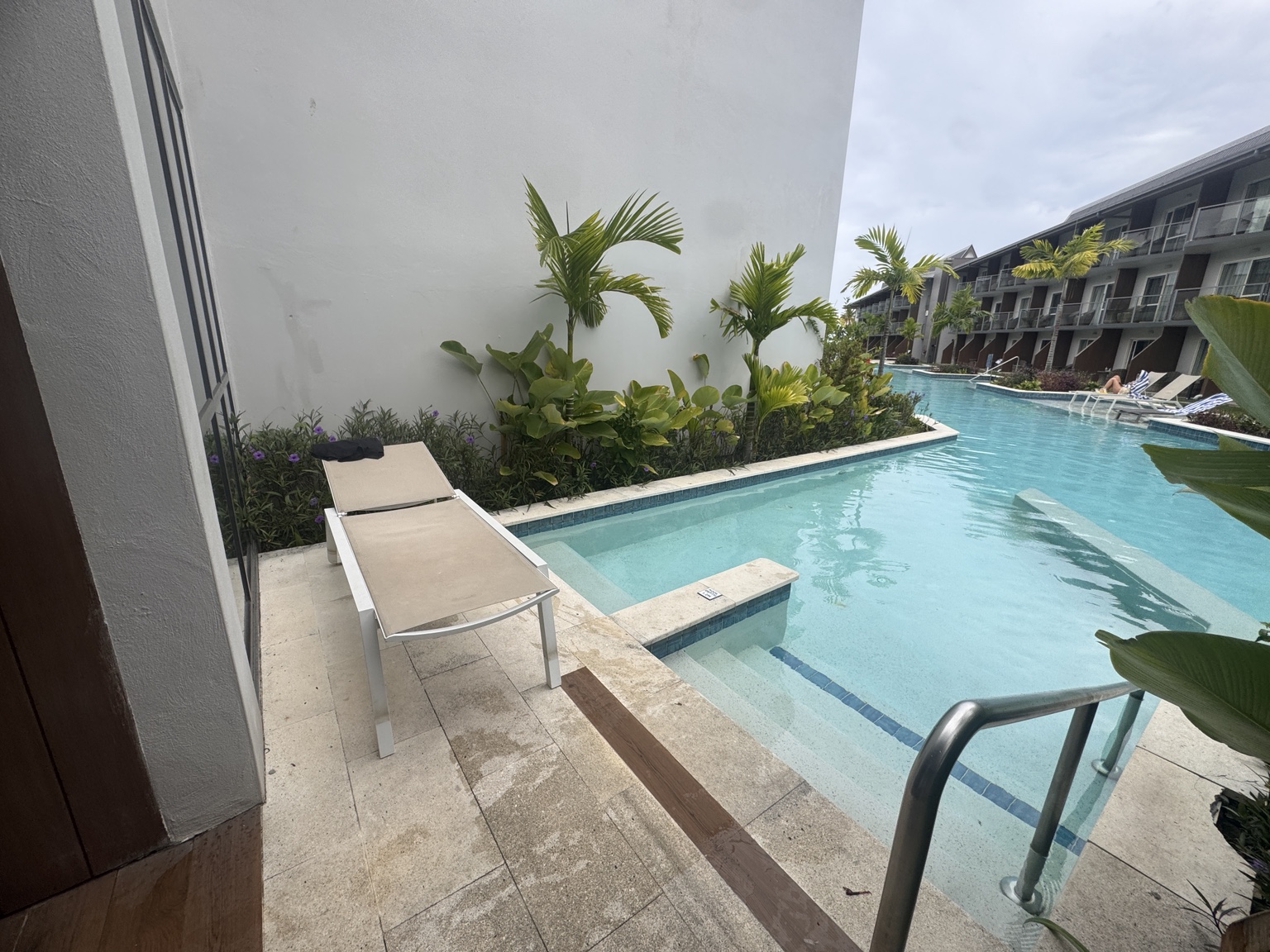 Our room patio with one sun lounger beside the pool and an accommodation block opposite